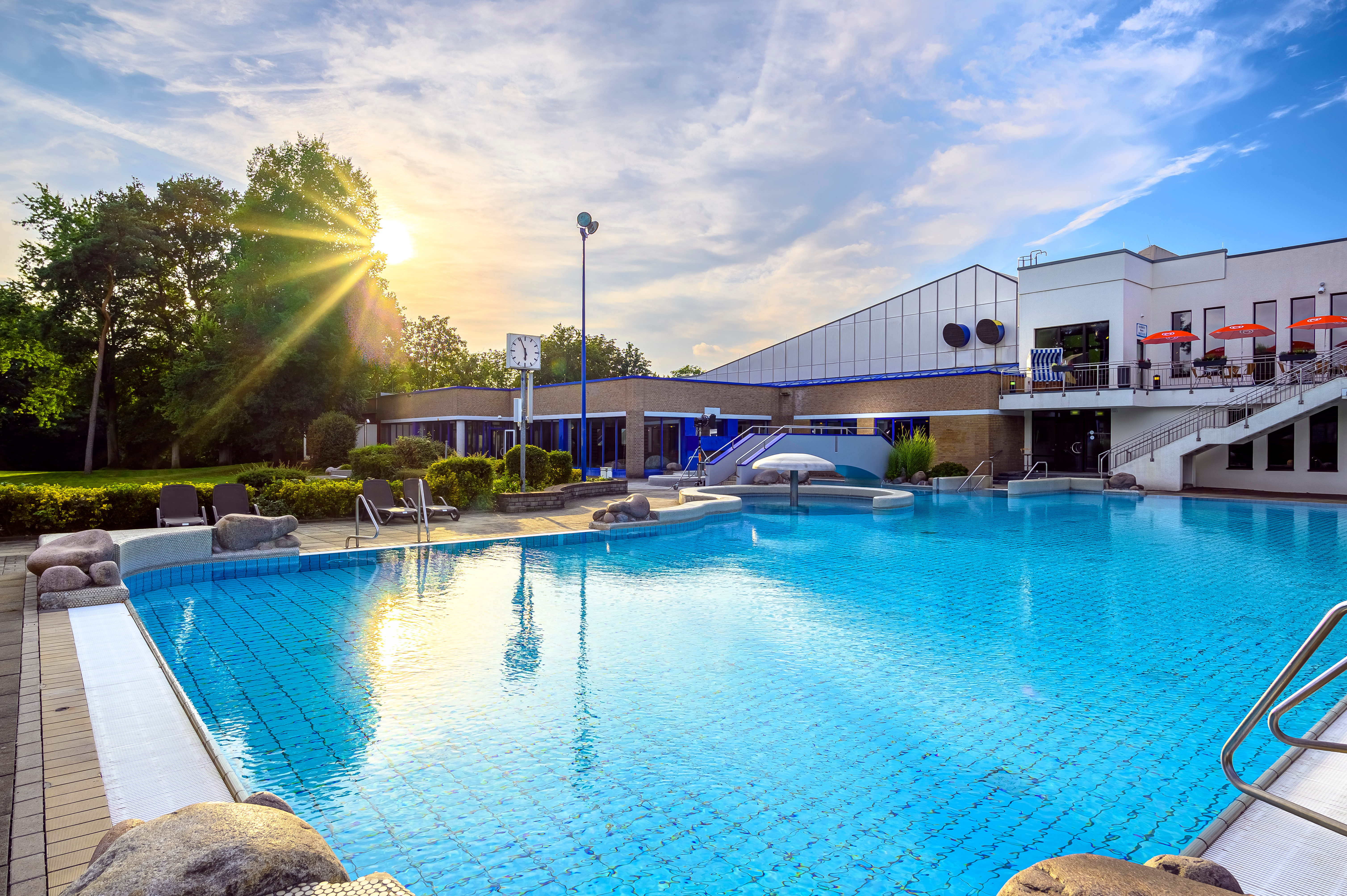 Das Bild zeigt einen sonnigen Tag an einem Schwimmbad, mit dem Wasser, das im Sonnenlicht glitzert.
