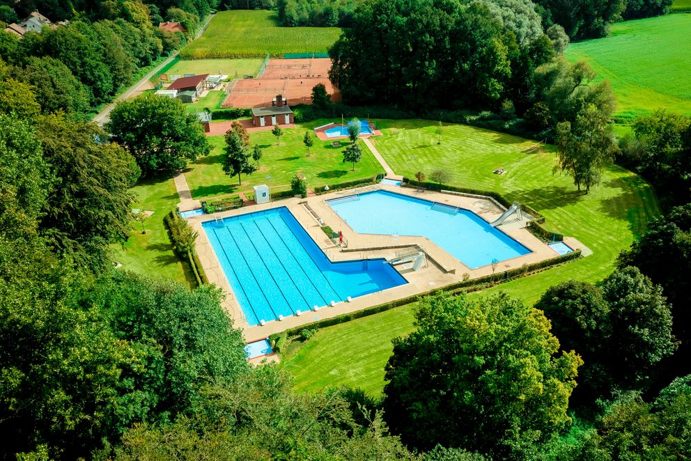 Freibad in naturnaher Umgebung. Das Bild zeigt ein idyllisch gelegenes Freibad mitten im Grünen. Zwei Becken, getrennt durch eine kleine Brücke, laden zum Schwimmen und Planschen ein – perfekt für entspannte Sommertage in der Natur.