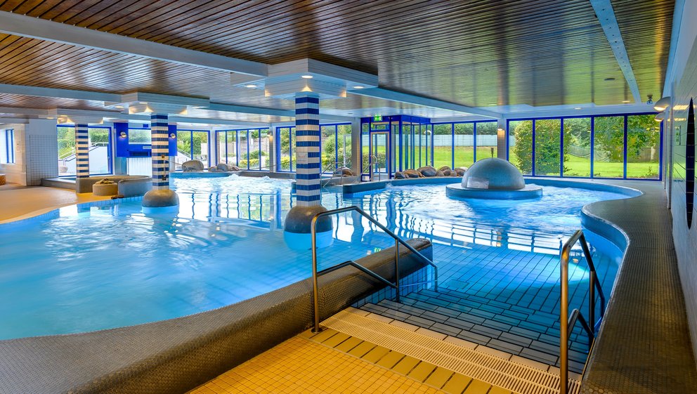 Modernes Hallenbad mit Holzarchitektur. Innenansicht eines Schwimmbads mit Holzdecke, das eine entspannende Atmosphäre und modernes Design vermittelt.