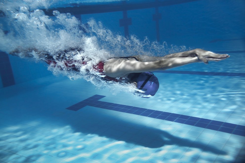 Schwimmer in Aktion unter Wasser. Das Bild zeigt einen Schwimmer in Aktion unter Wasser – kraftvoll gleitet er in gestreckter Haltung durch das Schwimmbecken. Die Szene steht für Dynamik, Technik und sportlichen Ehrgeiz.