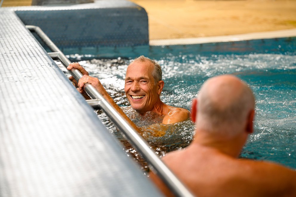 Zwei Männer genießen das Schwimmen im pool, während die Sonne auf die Wasseroberfläche scheint.