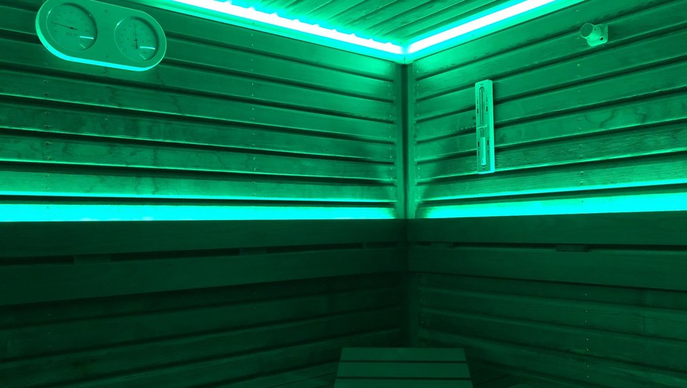 Sauna mit beruhigender grüner Beleuchtung. Innenansicht eines Saunaraums, beleuchtet von beruhigenden grünen Lichtern.