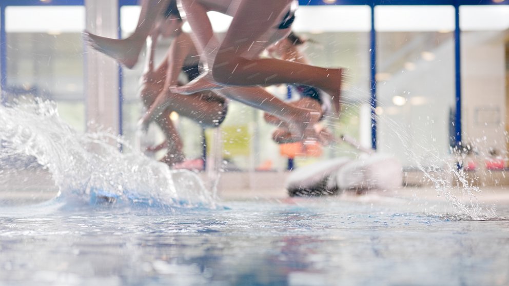 Das Bild zeigt mehrere Personen, die gleichzeitig ins Wasser springen. 