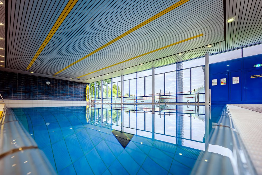 Trainingsbad mit tiefem Becken und Designdecke. Das Bild zeigt ein modernes Hallenbad mit einem tiefen Sprungbecken und mehreren Sprungbrettern. Die Architektur ist auffällig gestaltet – besonders die Decke mit grafischem Muster verleiht dem Raum eine besondere Atmosphäre. Ideal für Turmspringen und Trainingsbetrieb.