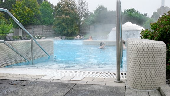 Das Bild zeigt ein dampfendes Außenbecken mit warmem Wasser, umgeben von Natur – ideal zum Entspannen an der frischen Luft.