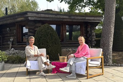 Frau Anje Evers und Frau Mechtild Schulze Hessing sitzen im Saunagarten vor der Panoramasauna.