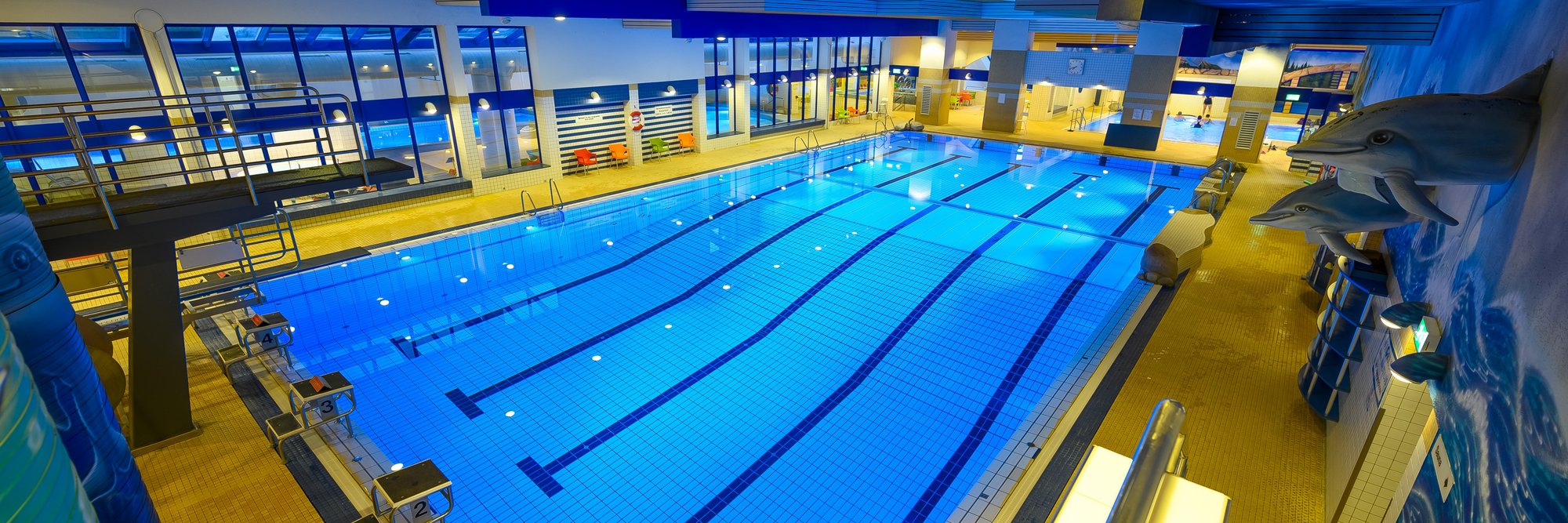 Modernes Hallenbad mit Wettkampfausstattung. Das Bild zeigt ein großes, modernes Hallenbad mit mehreren Schwimmbahnen, Startblöcken und Zuschauerplätzen – ideal für Training und Wettkämpfe.