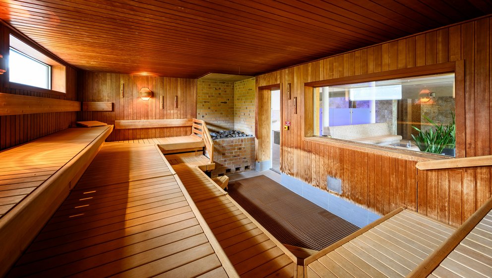 Ruhiger Saunabereich mit Holzverkleidung. Das Bild zeigt das Innere einer Sauna, die mit Holzverkleidung ausgestattet ist. Die Bänke sind ordentlich angeordnet und bieten viel Platz zum Entspannen.