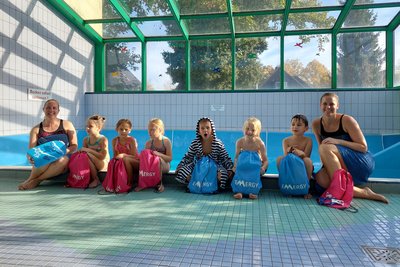 Das Bild zeigt eine Gruppe von acht Personen – darunter Kinder und Erwachsene – in einem Schwimmbecken.